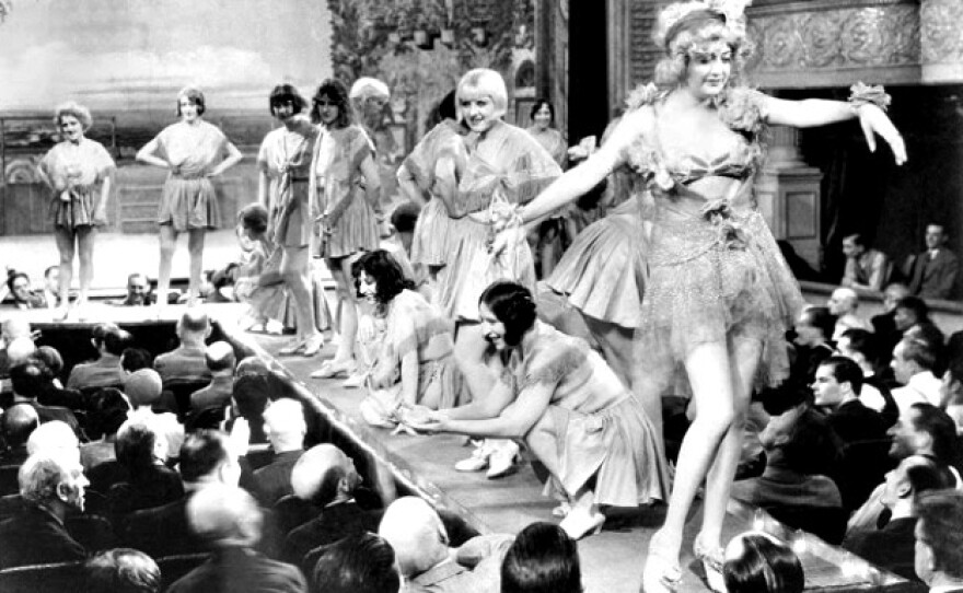 A black and white photograph showing a scene from the 1929 movie Applause directed by Rouben Mamoulian, featuring several showgirls performing on a raised stage before a seated theater audience.