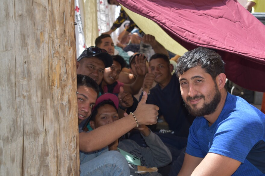 A group of people sit gathered outside underneath the shade of some blankets.