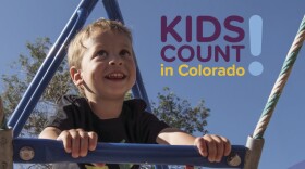 A small boy climbs a blue jungle gym with a clear sky above. The image is labeled, "KIDS COUNT in Colorado: 2026 Data Book - Colorado Children's Campaign."