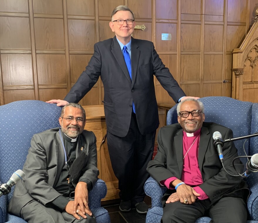 Bishop Jos Tharakan (left) and Bishop Michael Curry (right) visit with Morning Edition host George Prentice