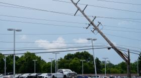 A snapped power pole hangs over a car lot 