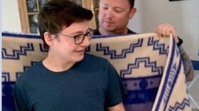 James's father holds a traditional tribal blanket in white and blue and drapes it over his son's shoulders.