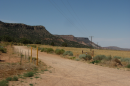 A dirt road near a yellow field with mountains in the near foreground, stretching off into the background.