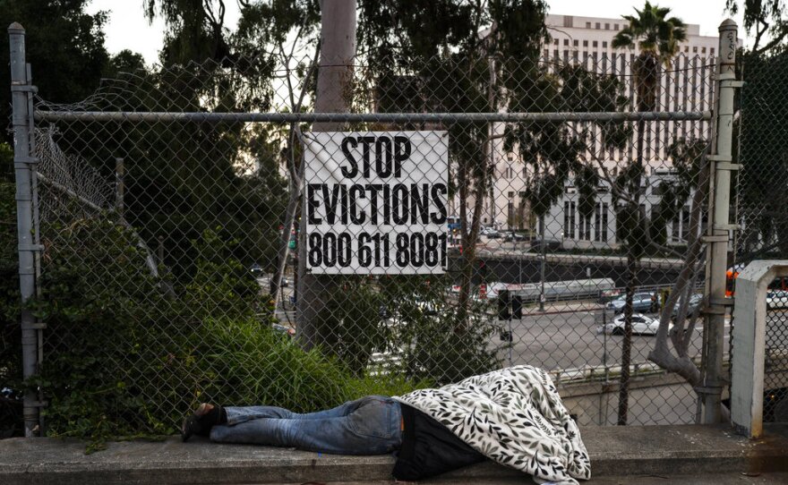 A homeless person sleeps on a sidewalk in Los Angeles, Monday, Feb. 13, 2023. Homelessness remains hugely visible throughout California with people living in tents and cars and sleeping outdoors on sidewalks and under highway overpasses.