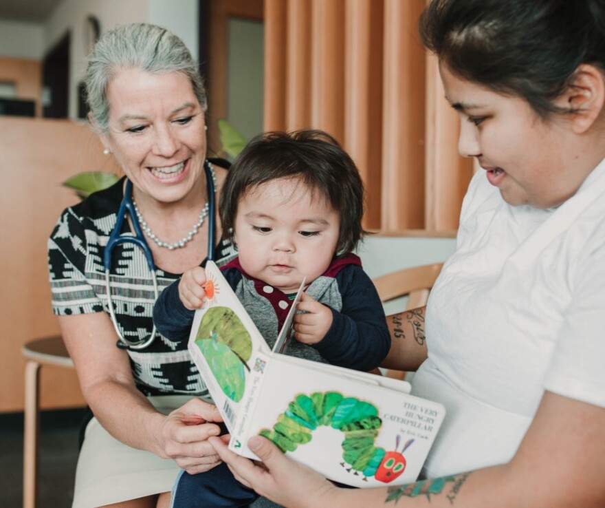 Baby is engaged in a book at a pediatrician's office while sitting on mother's lap