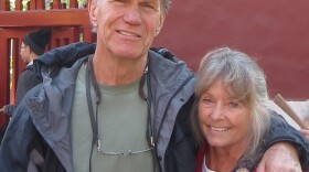 A man and woman stand together, the man has his arm around the woman. 