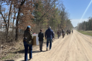 A long line of people walk away from the camera on a dirt road.
