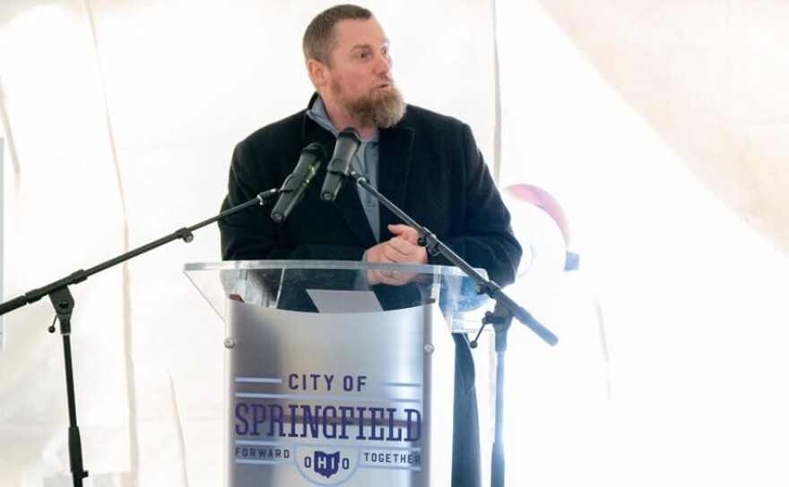 A man stands at a grey podium with the words "City of Springfield" on it. There's two microphones and a white background.