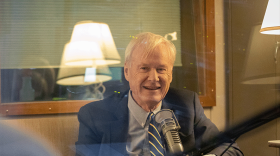 Chris Matthews sits in front of a microphone. He is smiling and holding a mug.