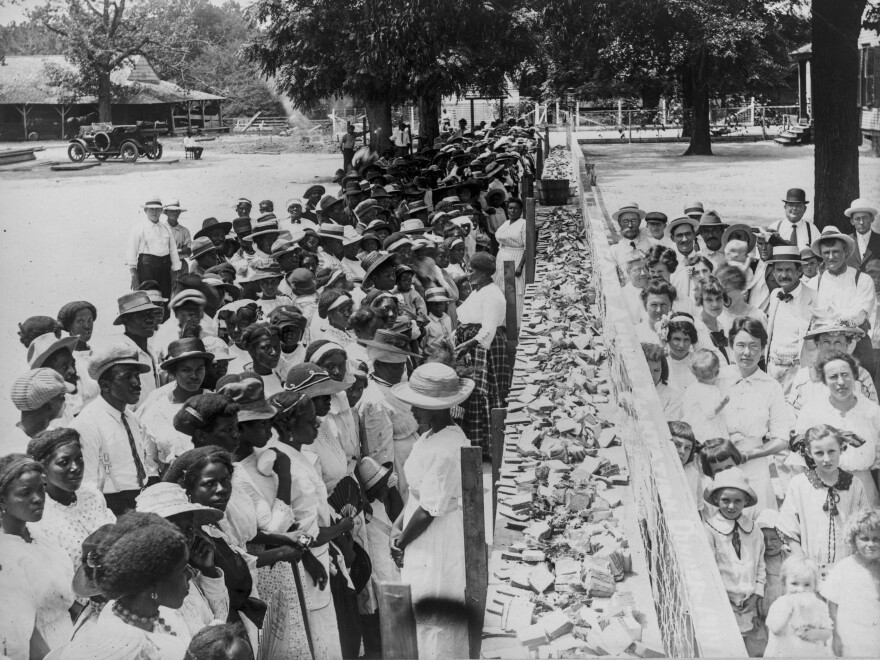 Crowds of African-American and white people are separated by a long counter covered with slices of bread at F.M. Gay's annual barbecue, held on his plantation every year in Alabama.