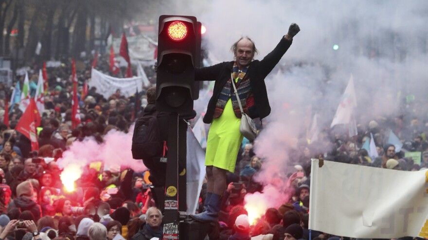 A man perched on a traffic light pumps his fist amid the chaos of a demonstration Thursday in Paris. Several thousand protesters took part in open-ended nationwide strikes, begun Thursday under union leadership.