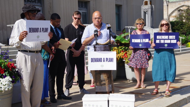 City Action and Kalamazoo Forward spokesperson Azlan Ibrahim speaks at a press conference on the steps of Kalamazoo City Hall on July 1, 2026, announcing the submission of signatures to the Kalamazoo City Clerk to put a Healthcare Action Plan on the city of Kalamazoo November ballot.