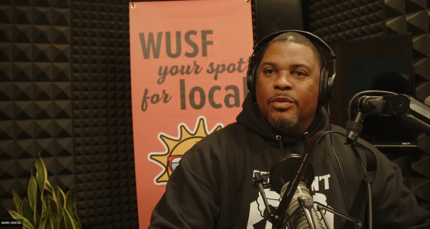 African American man sits by microphone with headphones on 