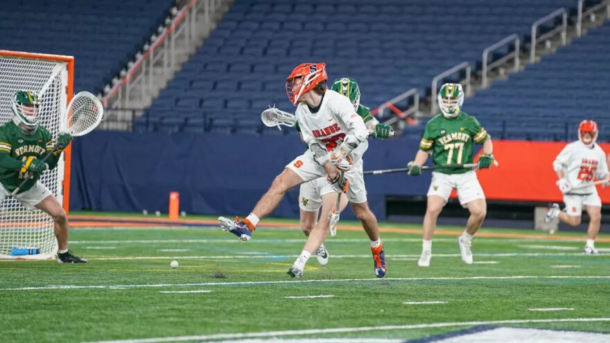 Syracuse attackman Finn Thomson (23, white) shoots between his legs and scores to advance the Orange lead against Vermont.