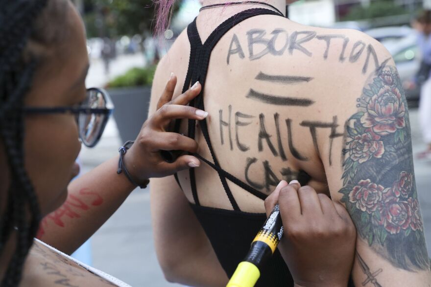 woman writing "abortion = health care" on another woman's back