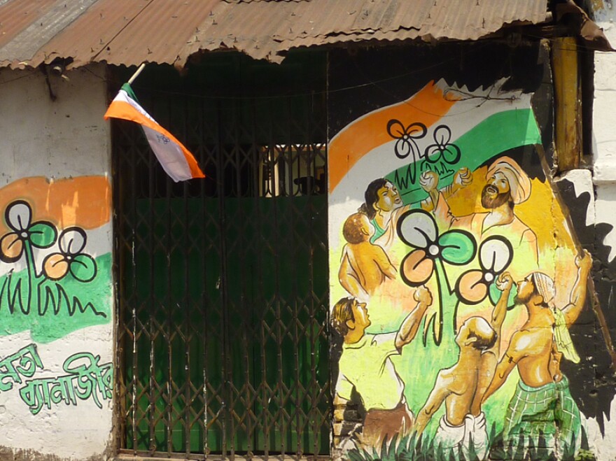 A house on a small side street in Calcutta is adorned with election graffiti. The Trinamool Congress logo looks like a three-leaf clover.  The name of the party's candidate, Mamata Banerjee, is written in Bengali on the lower left.