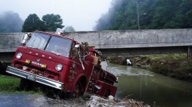 A fire truck is seen hangin over the edge of the water propped against a bridge on Wednesday, Aug. 3, 2022, in Hindman, Ky., after massive flooding carried the fire truck towards the water. Temperatures are soaring in a region of eastern Kentucky where people are shoveling out the wreckage of massive flooding. (AP Photo/Brynn Anderson)