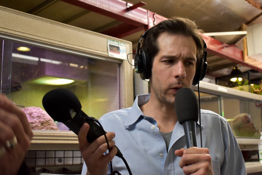 Man in headphones speaks into microphone and holds another