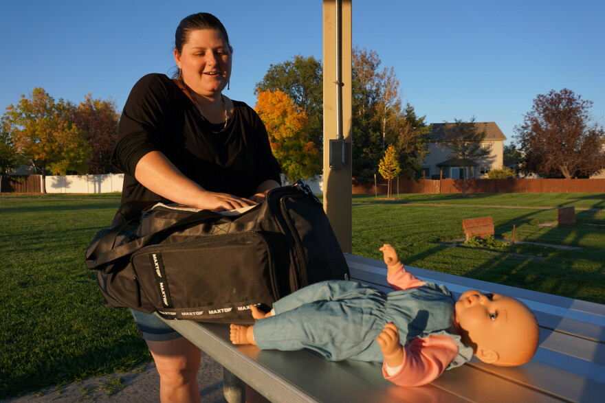  A woman riffles through a black duffel bag on top of a park table, with a babydoll on it.