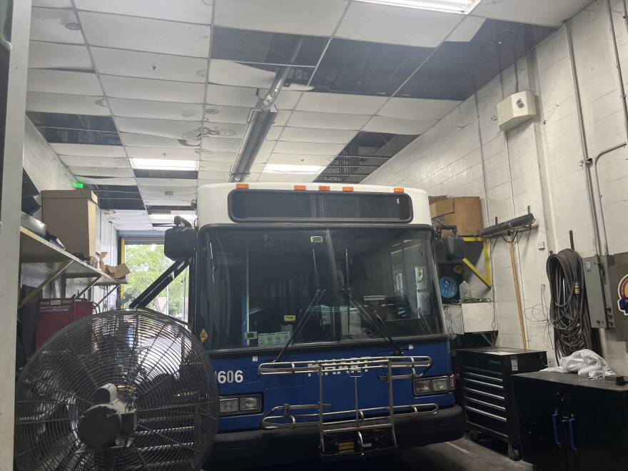 A bus in a narrow bay, where storms have knocked out many of the ceiling tiles and exposed the structure of the roof. 