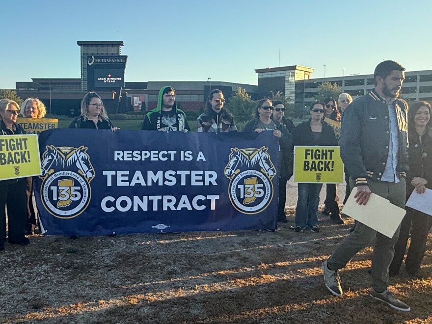 Men and women stand close together wearing jackets and coats. They are holding yellow and blue signs in their hands. Some of them say "Fight Back" "Respect is a Teamster Contract" 