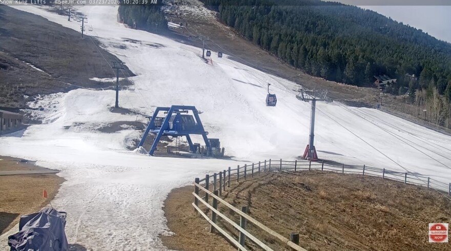 A patchy ski hill made up of some snow, dirt and grass.