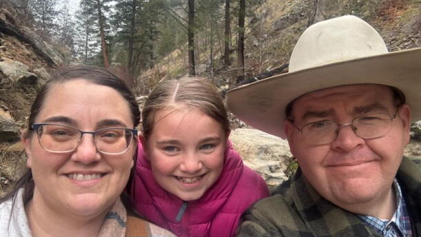 Tara Benson, Grace Benson and Jake Benson are framed together in a family photo with a mountainous background with green trees. 