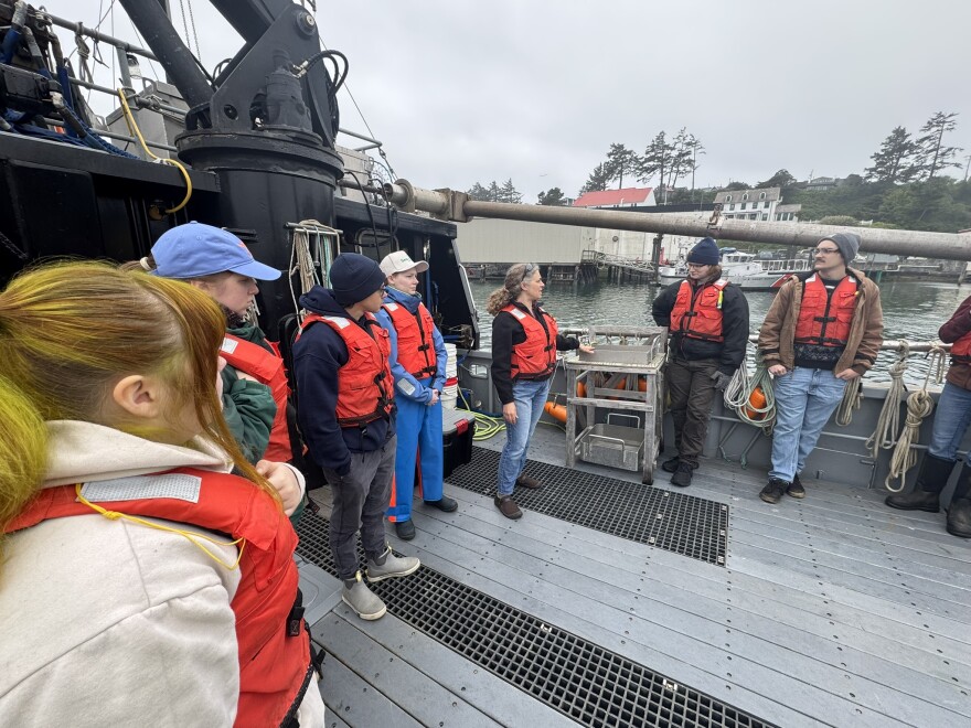 People on the deck of a boat listen to instructions from a professor.