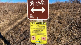 a tick warning is posted below a sign for the hank aaron state trail. it's a sunny late winter day.