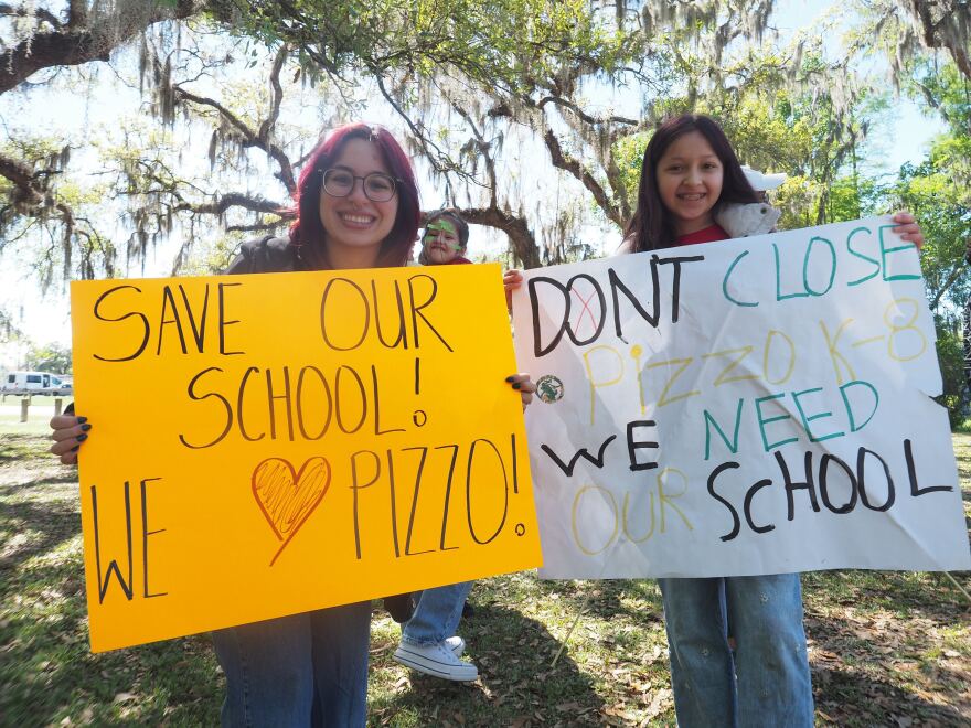 a teacher and student hold signs defending Pizzo K-8