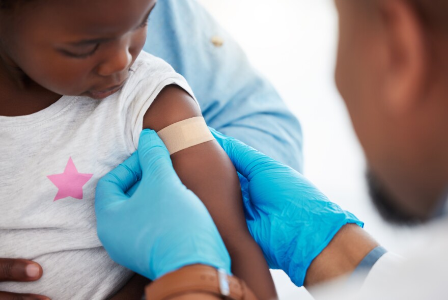 Doctor puts a bandage on a young girl's arm at the site where he injected a vaccine.