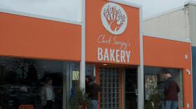 Customers stand at the entrance of Chef Sergey's Bakery at the grand opening in Midland, Mich., Saturday, Jan. 18, 2025. The exterior of the bakery stands out with its vibrant orange and aroma of fresh pastries.