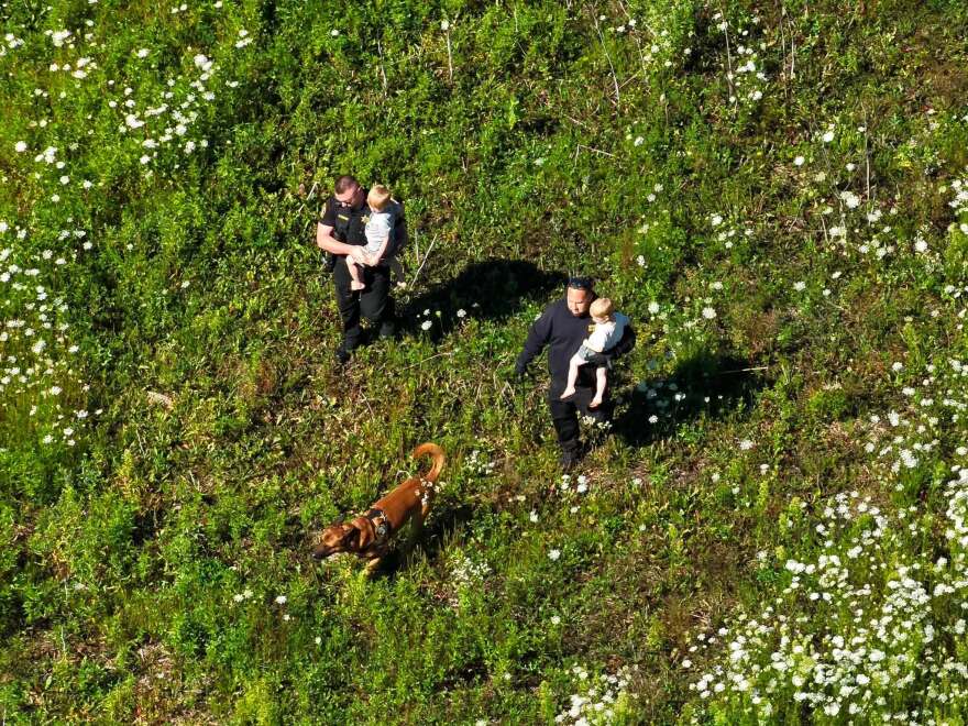 Menominee County Sheriff's deputies and K-9 Kado carry two children away from a field