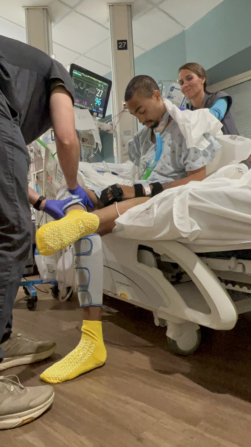 Calvin "Elijiah" Briggs sits on the edge of a hospital bed wearing yellow socks and a hospital gown.