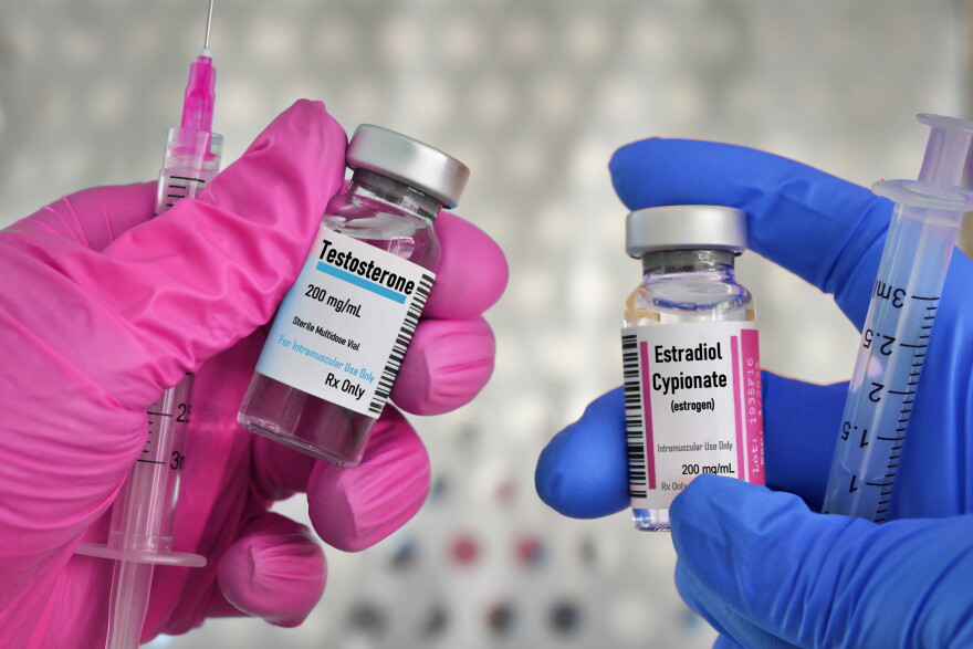 Gloved hands holding vials of testosterone and estrogen and syringes