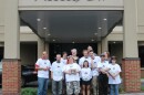 A dozen caregivers and clients stand in front of the Access CNY's brick and stucco building smiling while they hold an award recognizing its Self-Service Advocacy Club. 