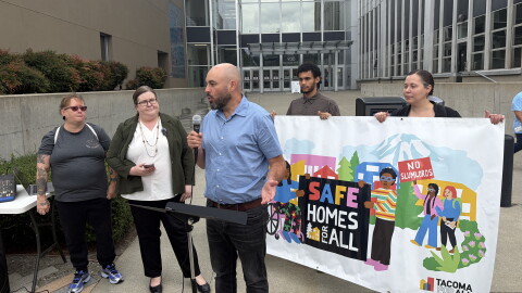 People stand at a press conference in front of a Tacoma court house. They have a banner that reads "Safe Homes For All" 