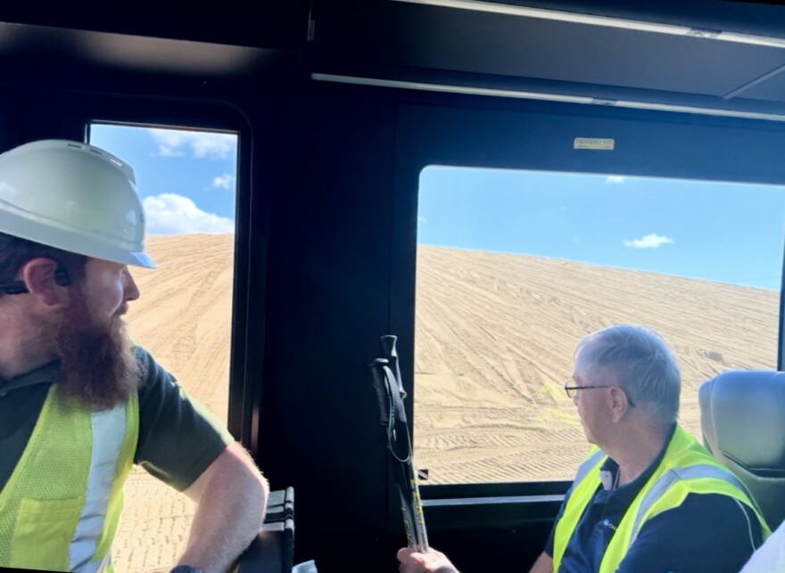People in hard hats and vests look out the window of a vehicle