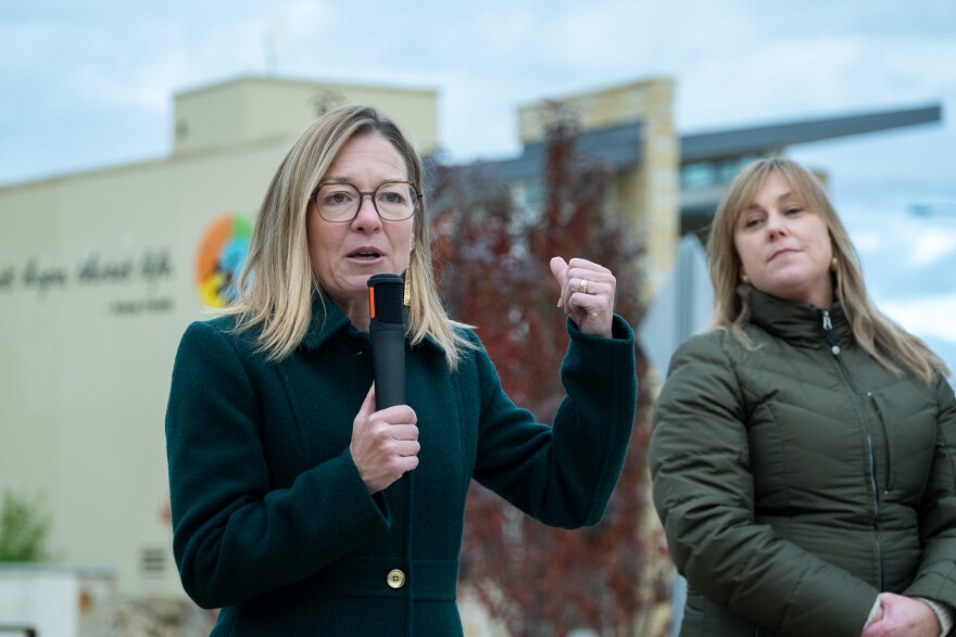 Two women dressed in coats speaking in front of a building.