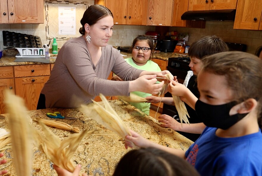 Woman helping young people tie corn husks together