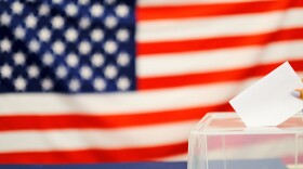 woman putting a ballot in a ballot box on election day. Close up of hand with white votes paper on usa flag background