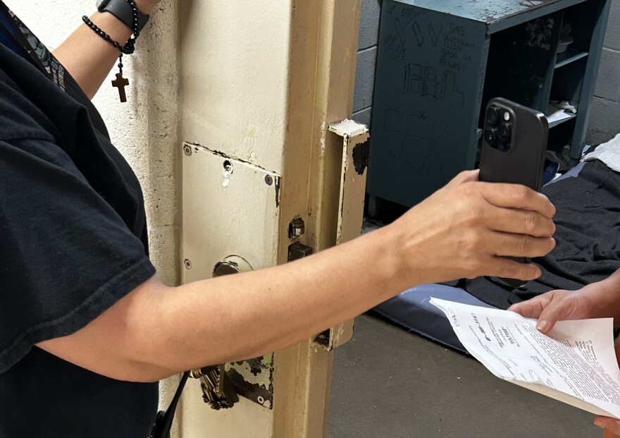 A detention officer at the Oklahoma County jail holds a phone up for a detainee for a virtual court hearing.