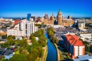 Aerial view of San Antonio's downtown skyline with the Riverwalk and lush trees in the foreground.