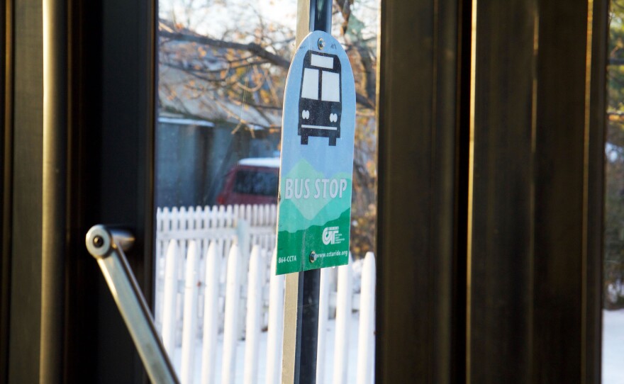 A bus stop sign seen through a bus door window.
