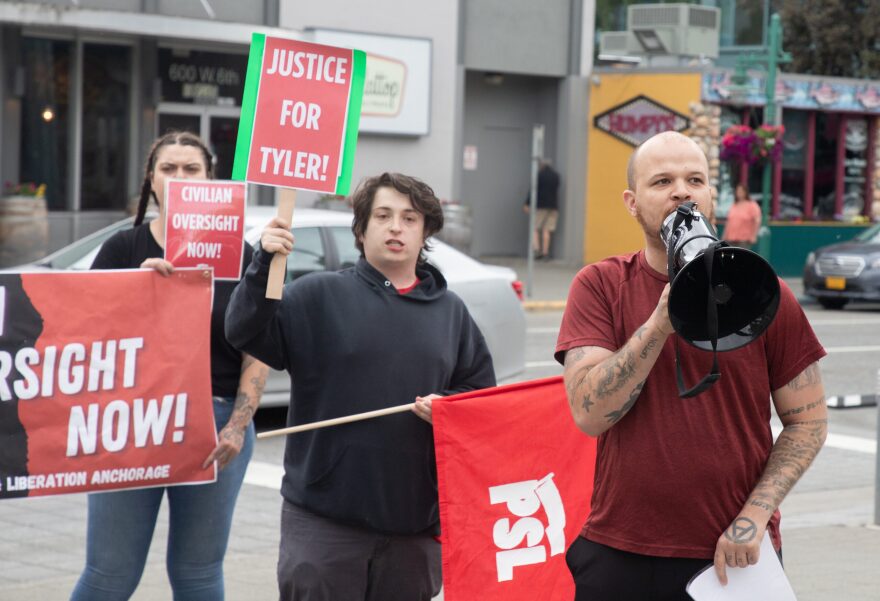 A man in a red shirt speaks into a a black megaphone.