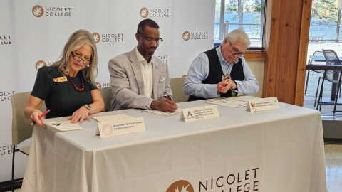 Nicolet College President Kate Ferrell, Director of the Wisconsin Bureau of Apprenticeship Standards David Polk, and Sokaogon Chippewa Community Chairman Robert VanZile sit at a table at the college signing an agreement that will launch a Broadband Service Technician apprenticeship program.