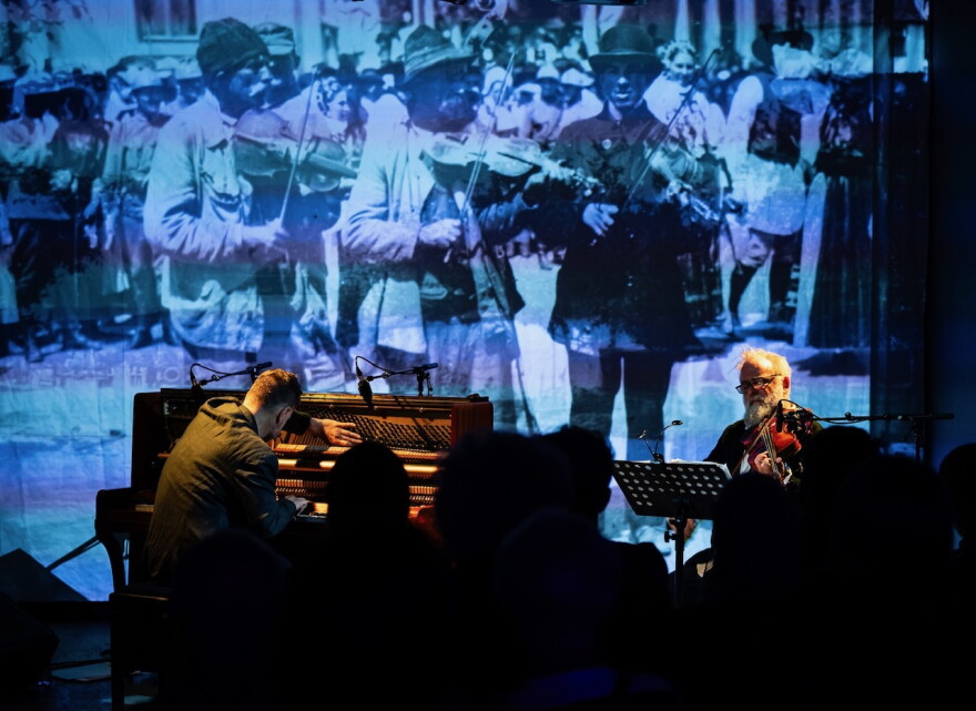 Maneri and Ban performing with an image of Transylvanian Folk Dance musicians from Bartok's filed research in the background.