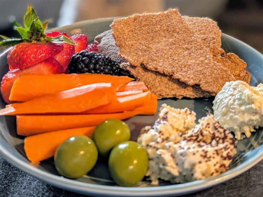 A plate of snacks like carerots, olives, cheese spreads and homemade bran crispbread.
