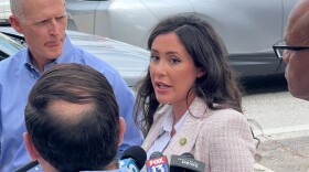 Woman with dark hair speaking to reporters