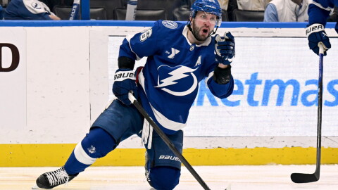 Hockey player in a blue uniform with a lightning bolt on the front with his knee on the ice and fist in the air celebrating